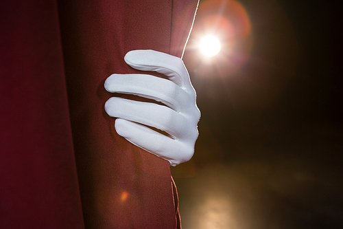 Close-up of hand in a white glove pulling curtain away