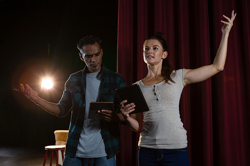 Actors rehearsing on stage while using digital tablet in theatre