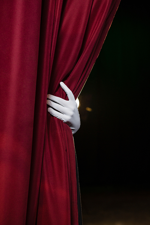 Close-up of hand in a white glove pulling curtain away