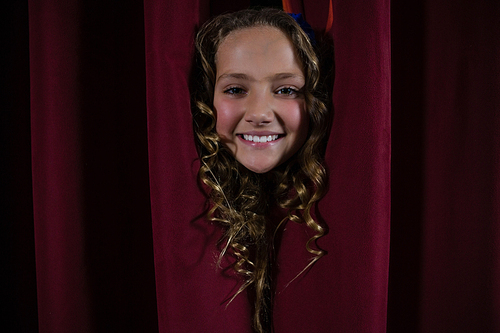 Portrait of smiling female artist peeking through the red curtain