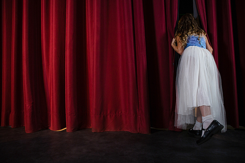 Rear view of female artist peeking through the red curtain