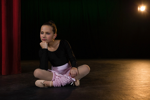 Thoughtful ballerina sitting on the stage in theatre