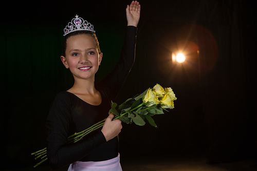 Happy ballerina posing with flower bouquet on stage in theatre