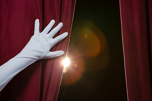 Close-up of hand in a white glove pulling curtain away