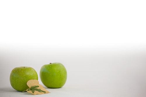 Close-up of green apples and autumn leaves against white background