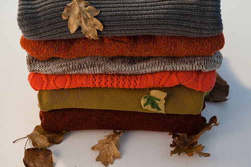 Stack of woolen clothing with autumn leaves on white background