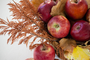 Close-up of red apples with autumn leaves in wicker basket against white background