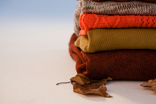 Stack of woolen clothing with autumn leaves on white background