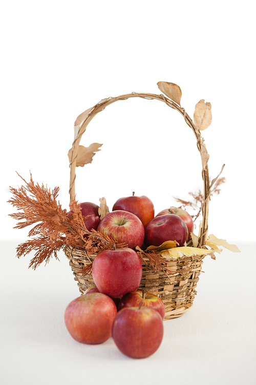 Close-up of red apples with autumn leaves in wicker basket against white background