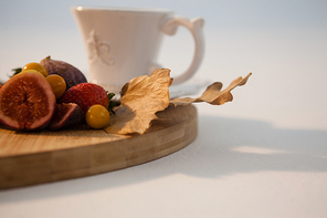 Autumn leaves, various fruits and cup of tea on chopping board against white background