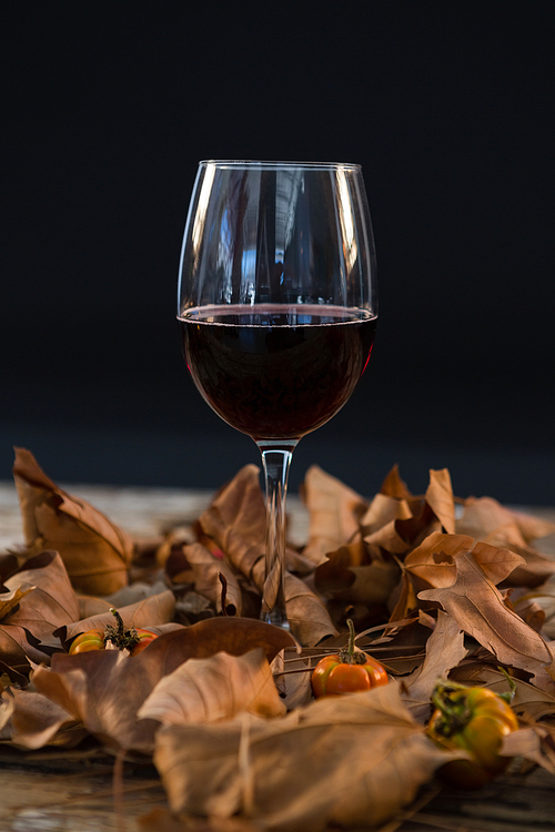 Wineglass glass amidst dry leaves on wooden table against black background