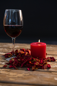 Wineglass by illuminated candle on wooden table against black background