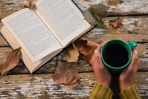 Cropped hand holding coffee cup by book on wooden table