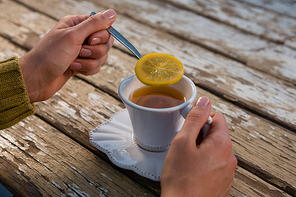 Cropped hands of woman holding lemon in spoon while having tea at wooden table