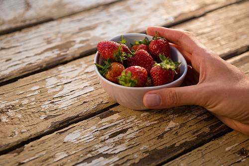 Cropped hand holding bowl containing strawberries at wooden table