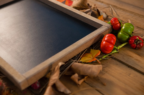 Close up of writing slate amidst dry leaves and tomato on wooden table
