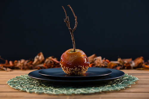 Close up of caramelized apple served in plate on wooden table against black background