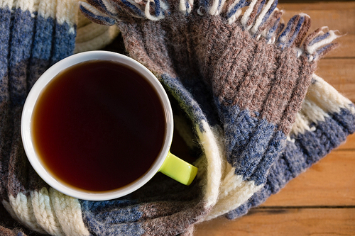Overhead view of black coffee amidst scarf on wooden table