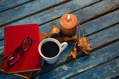 High angle view of tea cup with eyeglasses and books by illuminated candle on wooden table