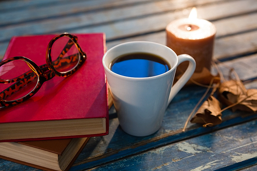 Close up of tea cup with eyeglasses and books by illuminated candle on wooden table