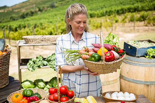 Happy woman holding fresh vegetables in basket at vegetable stall