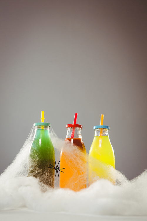 Drinks in bottles amidst cotton candy with artificial spider against gray background