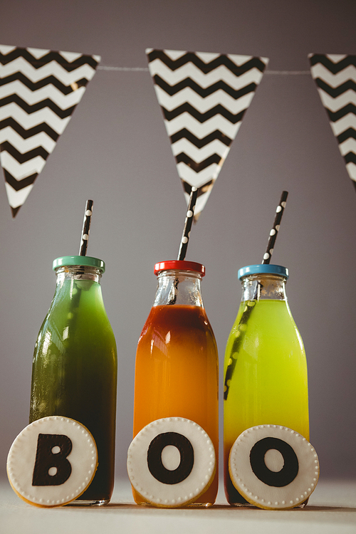 Cookies with boo text by colorful drinks in bottles against gray background