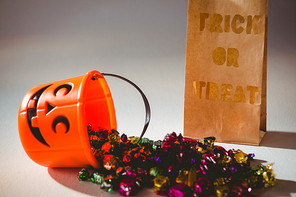 Trick or treat text on paper bag by bucket and colorful chocolates on white background