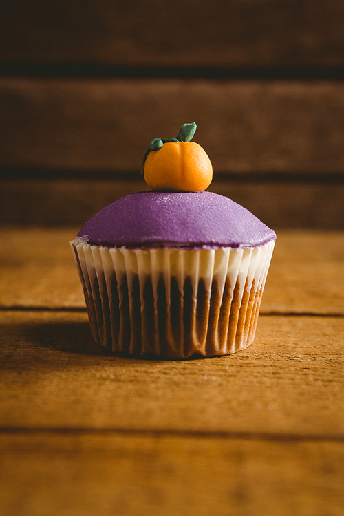 Close up of purple cup cake with pumpkin icing on wooden table