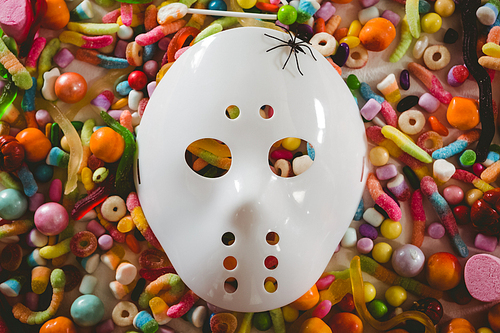 Overhead view of mask with various candies over white background