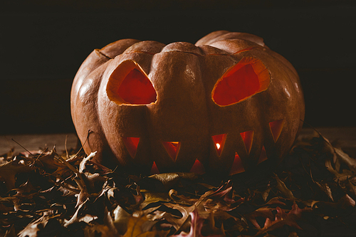 close up of illuminated jack o lantern with leaves on table during