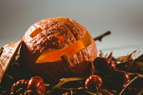 Close up of jack o lantern with small pumpkins and leaves over white background