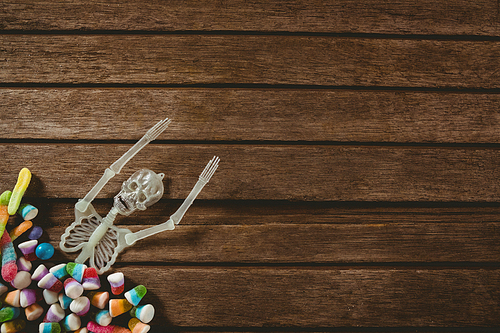 Overhead view of skeleton decoration with candies on wooden table