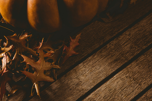 Cropped image of pumpkin with autumn leaves on wooden table