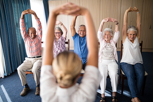 Cheerful senior men and women exercising with female doctor at retirement home