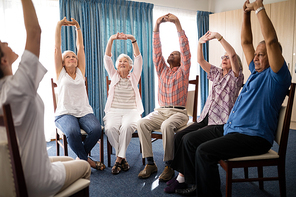 Seniors stretching with female doctor while sitting on chairs at retirement home