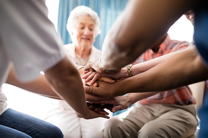 Cropped image of female doctor and senior people stacking hands at retirement home