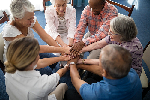 High angle view of female doctor amidst seniors stacking hands at retirement home