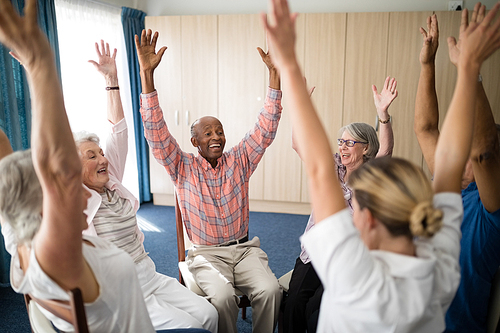 Cheerful seniors and female doctor sitting with raised hands at retirement home