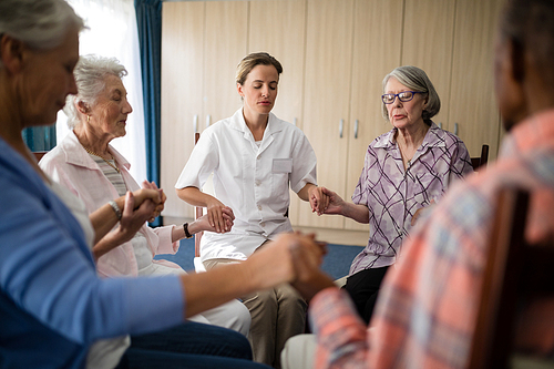 Female doctor meditating while holding hands with seniors at retirement home