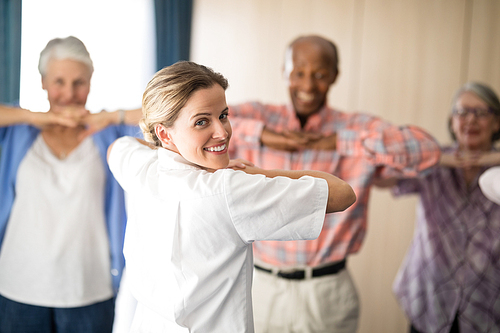 Rear view of smiling female doctor exercising with senior people at retirement home