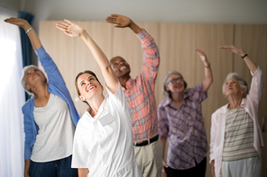 Smiling female doctor and seniors exercising with arms raised at retirement home