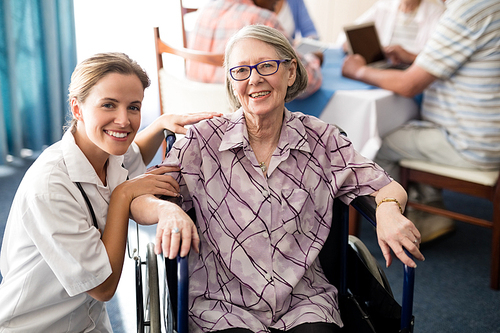 portrait of smiling female doctor with disabled senior woman sitting on . at retirement home