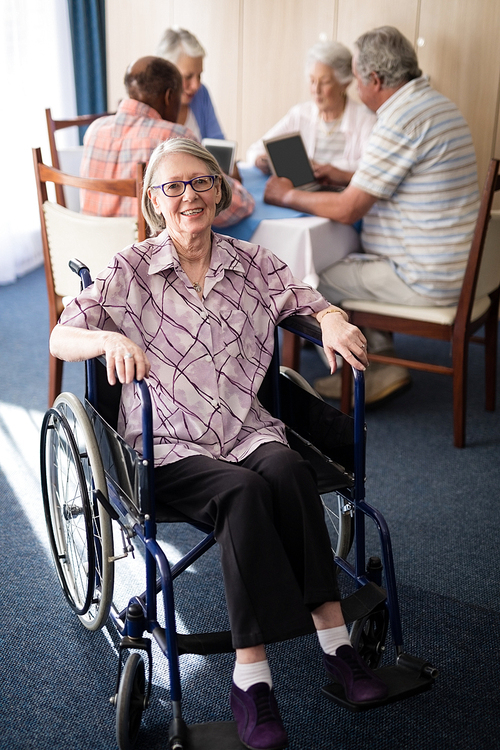 portrait of smiling disabled senior woman sitting on . against friends at retirement home