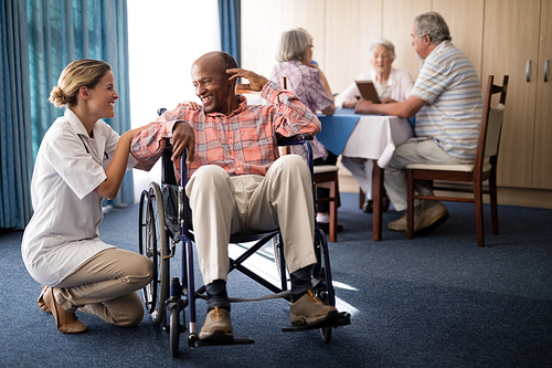 smiling female doctor kneeling by disabled senior man sitting on . at retirement home