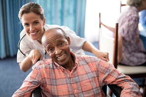 Portrait of cheerful female doctor standing with disabled senior man on wheelchair at retirement home