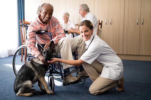 Portrait of smiling female doctor kneeling by disabled senior man stroking puppy at retirement home