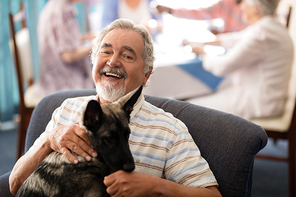 Portrait of smiling senior man sitting with puppy on chair at retirement home