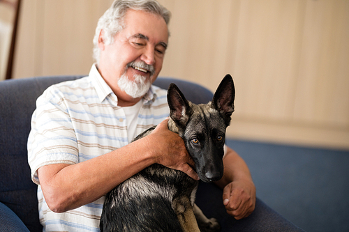 Happy senior man stroking puppy while sitting on armchair at retirement home