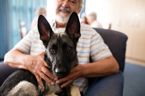 Midsection of senior man holding puppy while sitting on armchair at retirement home
